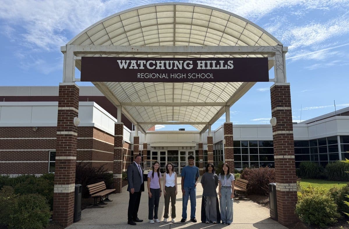 The five Watchung Hills Regional High School students named National Merit Semifinalists gather with a school administrator outside the school.